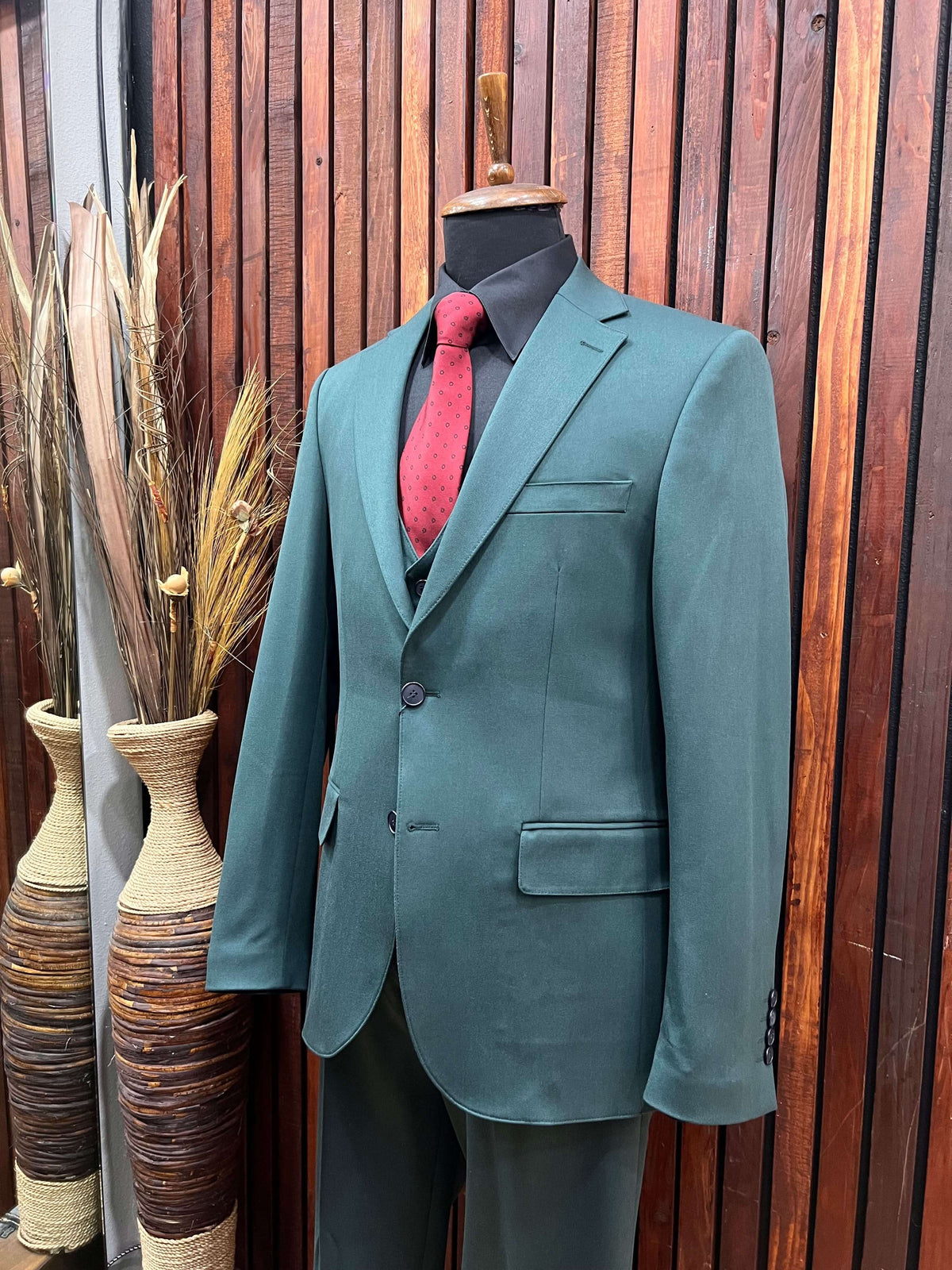 Men's forest green 3-piece slim fit suit displayed on a mannequin with a red tie and stylish decor.