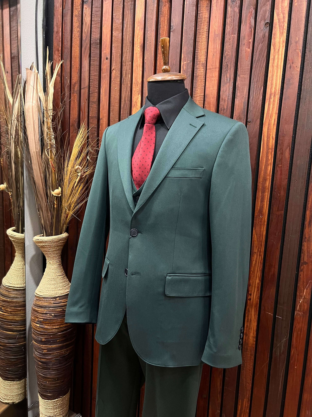 Men's forest green slim fit 3-piece suit with red tie displayed on a mannequin against wooden backdrop.